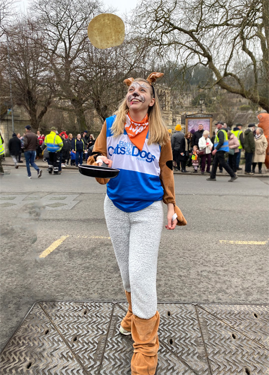 Katy in a dog outfit flipping a pancake for a Pancake Race 