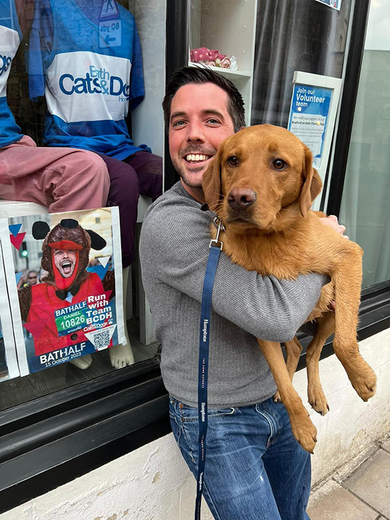 Dan Hill and his dog Basil outside our Charity Shop window featuring him running the Bath Half last year 